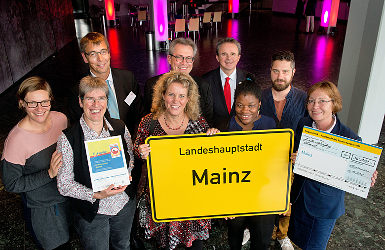 Eine Gruppe, die das Ortsnamensschild Mainz trägt, lächelt in die Kamera.